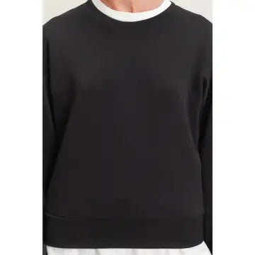 A black crewneck sweatshirt with a contrasting white ribbed collar, shown on a model.