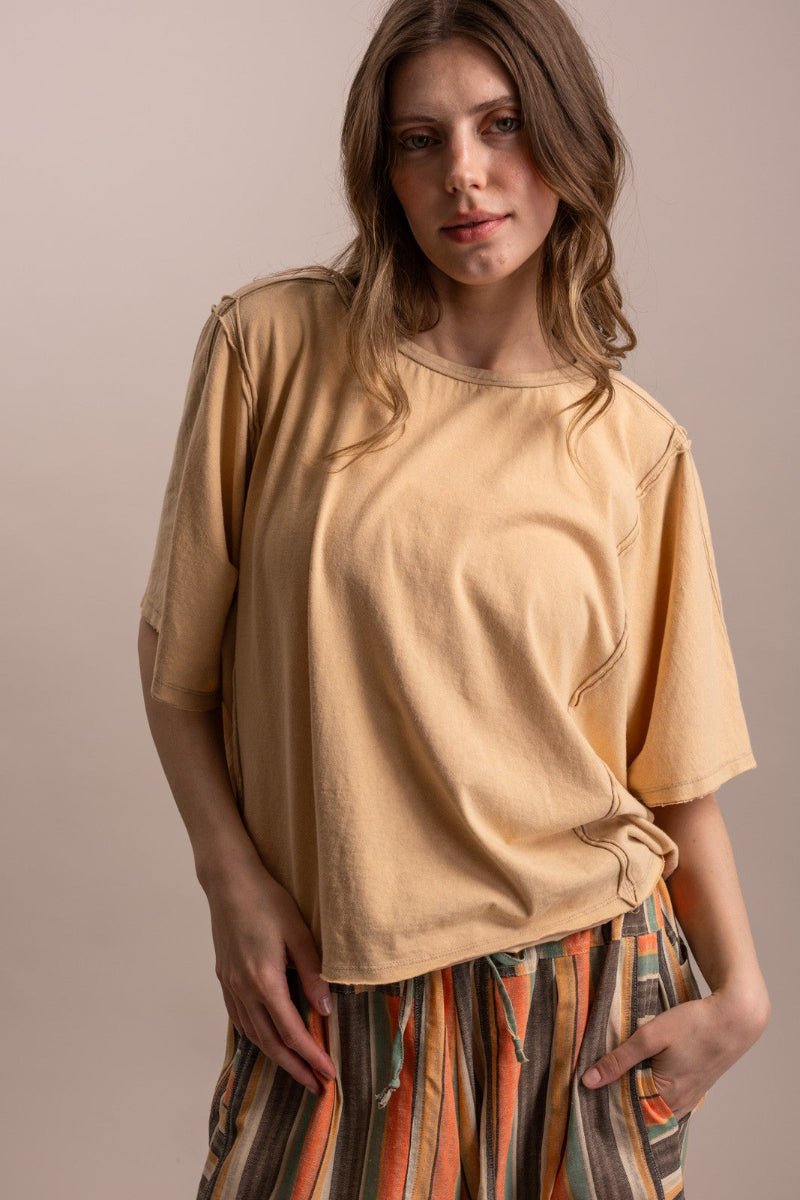 A woman wearing a loose, short-sleeve beige t-shirt and striped multicolor pants, standing against a solid light beige background.