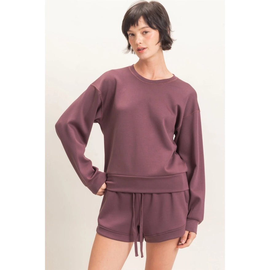 Woman wearing a mauve sweatshirt and shorts set on a plain background