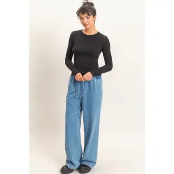 A woman modeling a black long-sleeve crewneck top and light blue wide-leg drawstring pants against a plain off-white studio background.