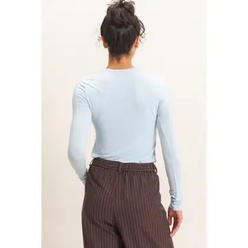 back view of a woman with her hair up wearing a light blue top and brown pants