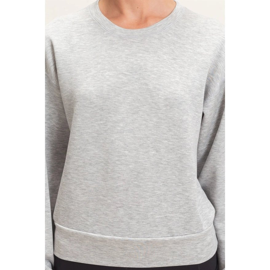 A close-up of a person wearing a light heather gray crewneck sweatshirt, showing the chest, collar, and lower hem against a plain light background.