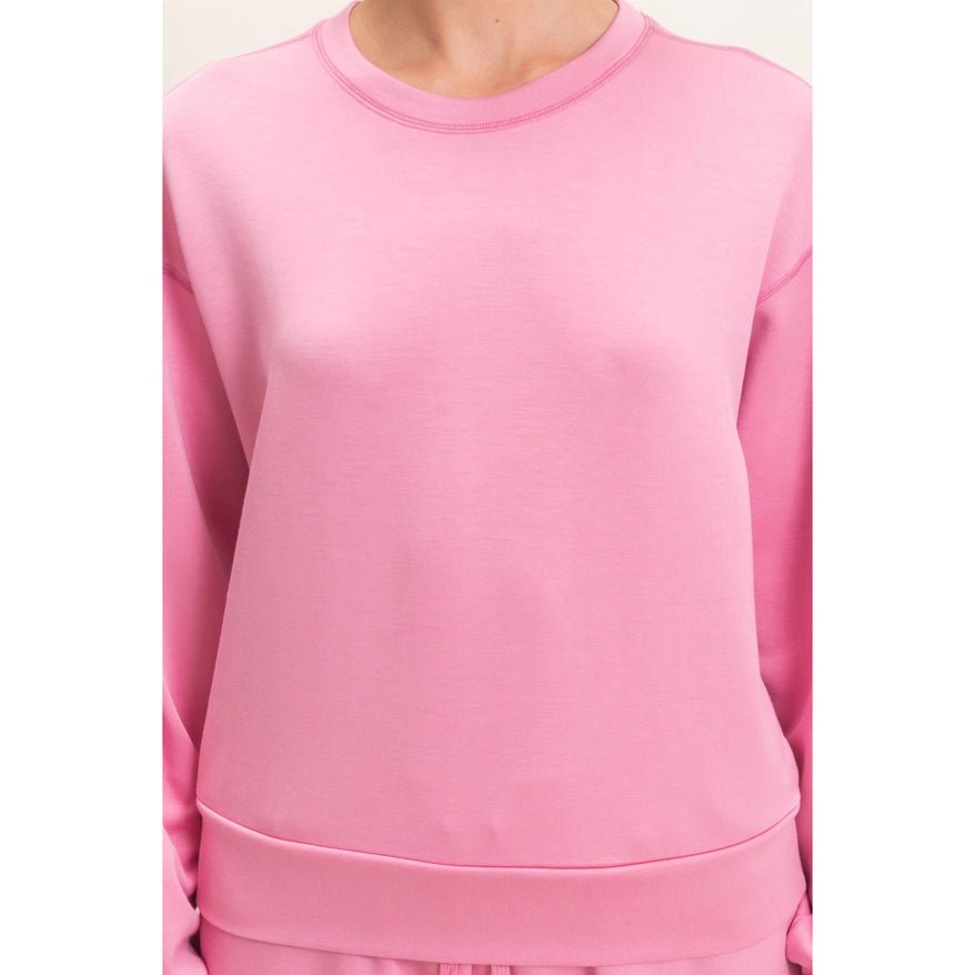 A close-up of a person wearing a solid pink crewneck sweatshirt, showing the chest, neckline, and a portion of the lower hem.