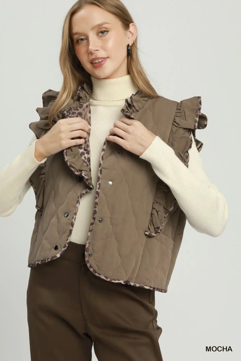 A woman wearing a brown ruffled quilted vest over a cream turtleneck sweater and brown pants, photographed against a light gray studio background. The word 'MOCHA' appears in the bottom right corner.