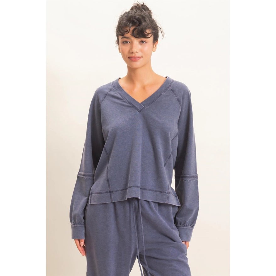 A woman modeling a matching two-piece lounge set consisting of a long-sleeve V-neck top and coordinating pants in a dusty slate blue color, set against a plain off-white background.