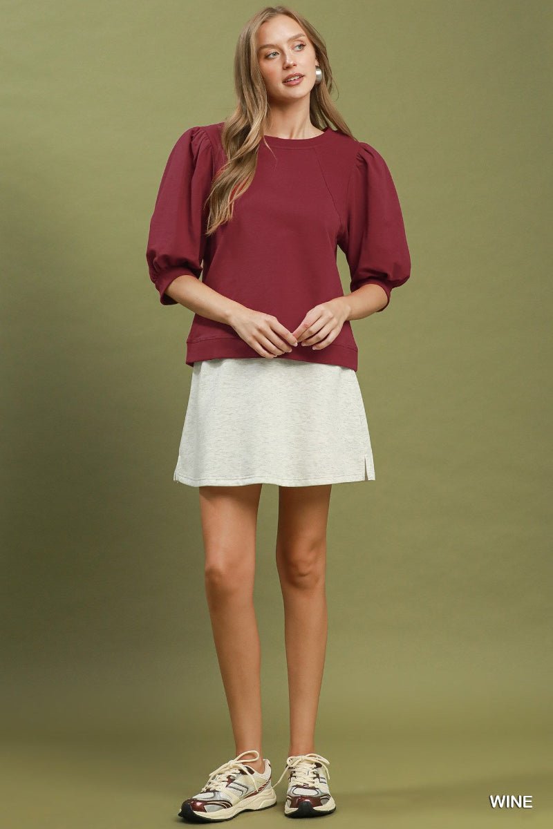 Woman wearing a burgundy top and white skirt on a green background