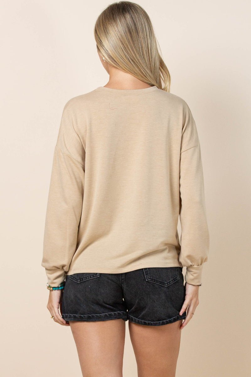 A woman shown from the back wearing a beige long-sleeve crewneck sweatshirt and dark denim shorts against a solid light beige background.