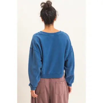 A person shown from the back wearing a cropped blue sweatshirt and dusty rose pants against a plain off-white background.