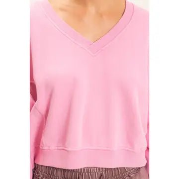 A close-up of a person wearing a light pink long-sleeve V-neck sweatshirt, paired with brown elastic-waist pants.