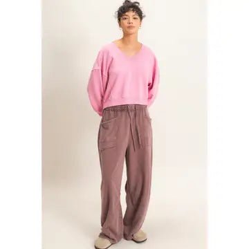 A model wearing a pink cropped V-neck sweatshirt and dusty rose wide-leg cargo pants, standing against a plain off-white studio background.