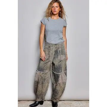 A woman modeling a light gray short-sleeve t-shirt and loose, wide-leg patchwork pants with a brown and beige abstract pattern, standing against a light gray wall.