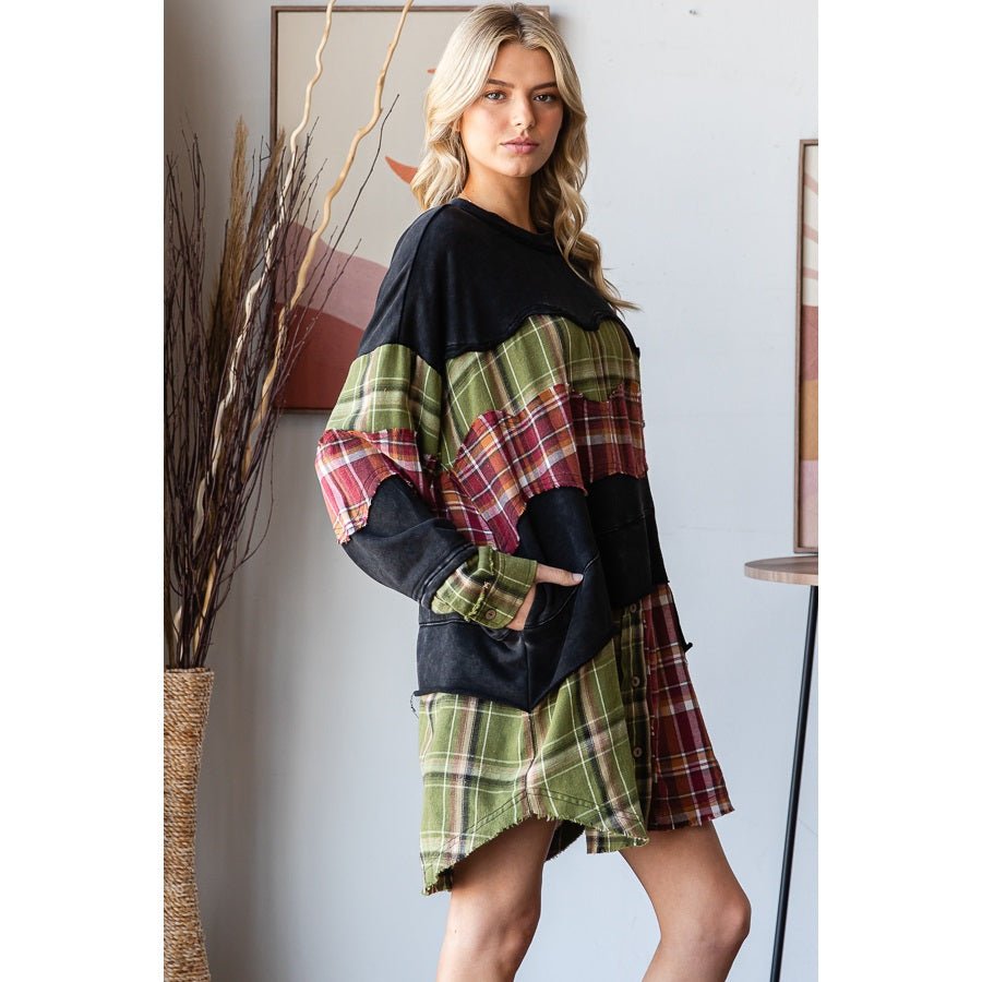 A woman models a patchwork long-sleeve mini dress with black knit fabric and green, red, and beige plaid panels, standing in a styled indoor setting.