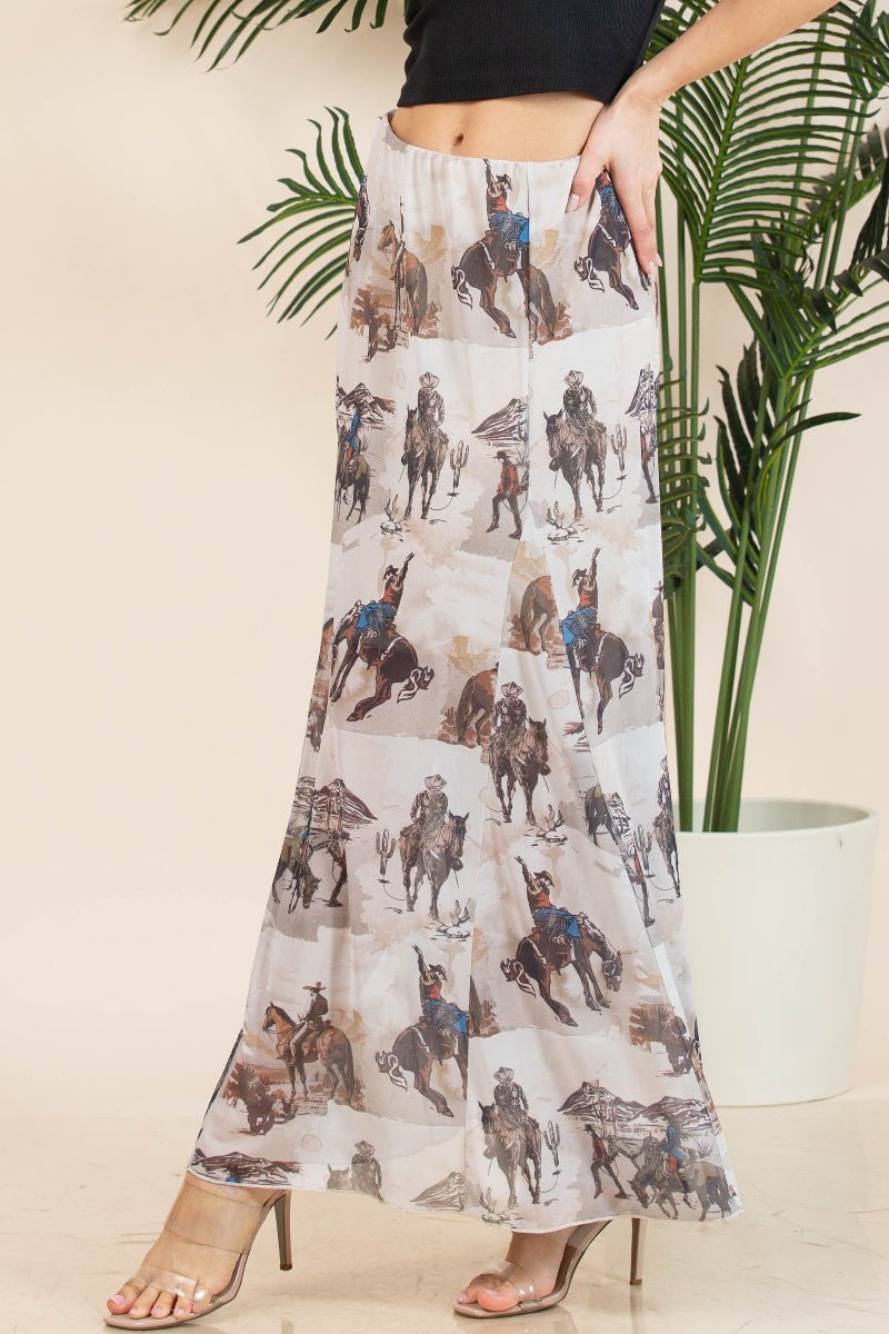 A woman models a long, wide-leg skirt featuring an all-over western print of cowboys on horseback. The skirt has a light beige base with brown, gray, and blue details in the printed illustrations.