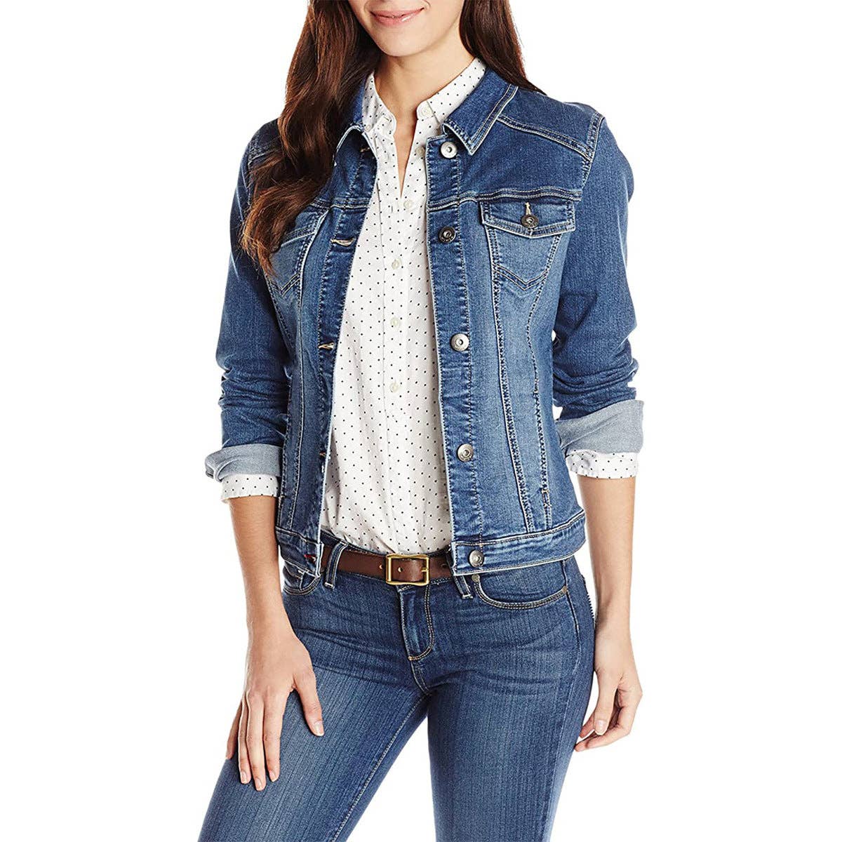 A woman wearing a blue denim jacket over a white polka-dot blouse and blue jeans, photographed against a plain white studio background.