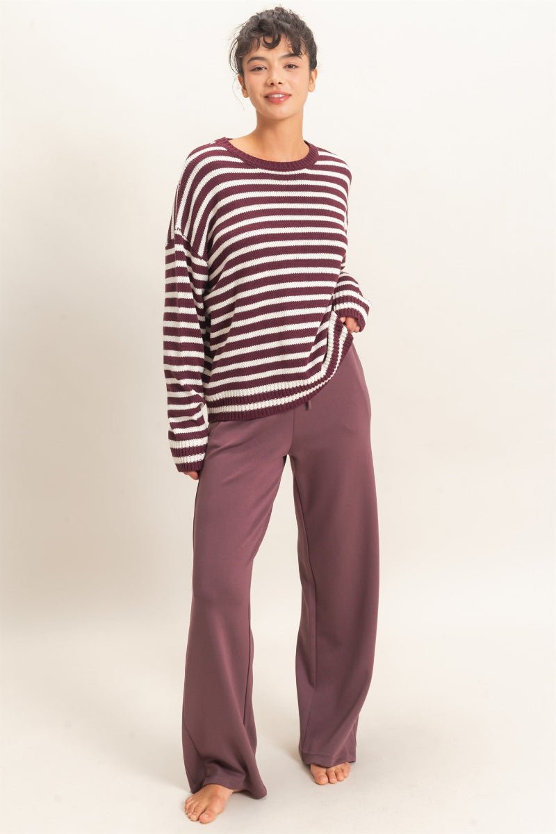 Person wearing a striped sweater and purple pants on a plain background