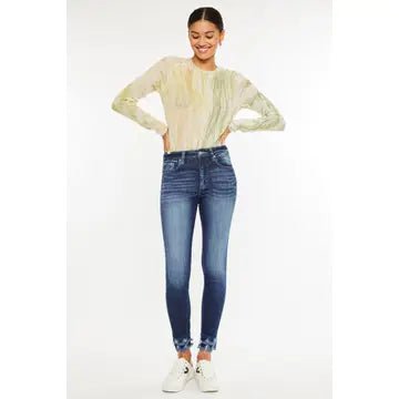 A woman modeling a pale yellow long-sleeve textured top and blue skinny jeans with white sneakers, standing against a plain white studio background.