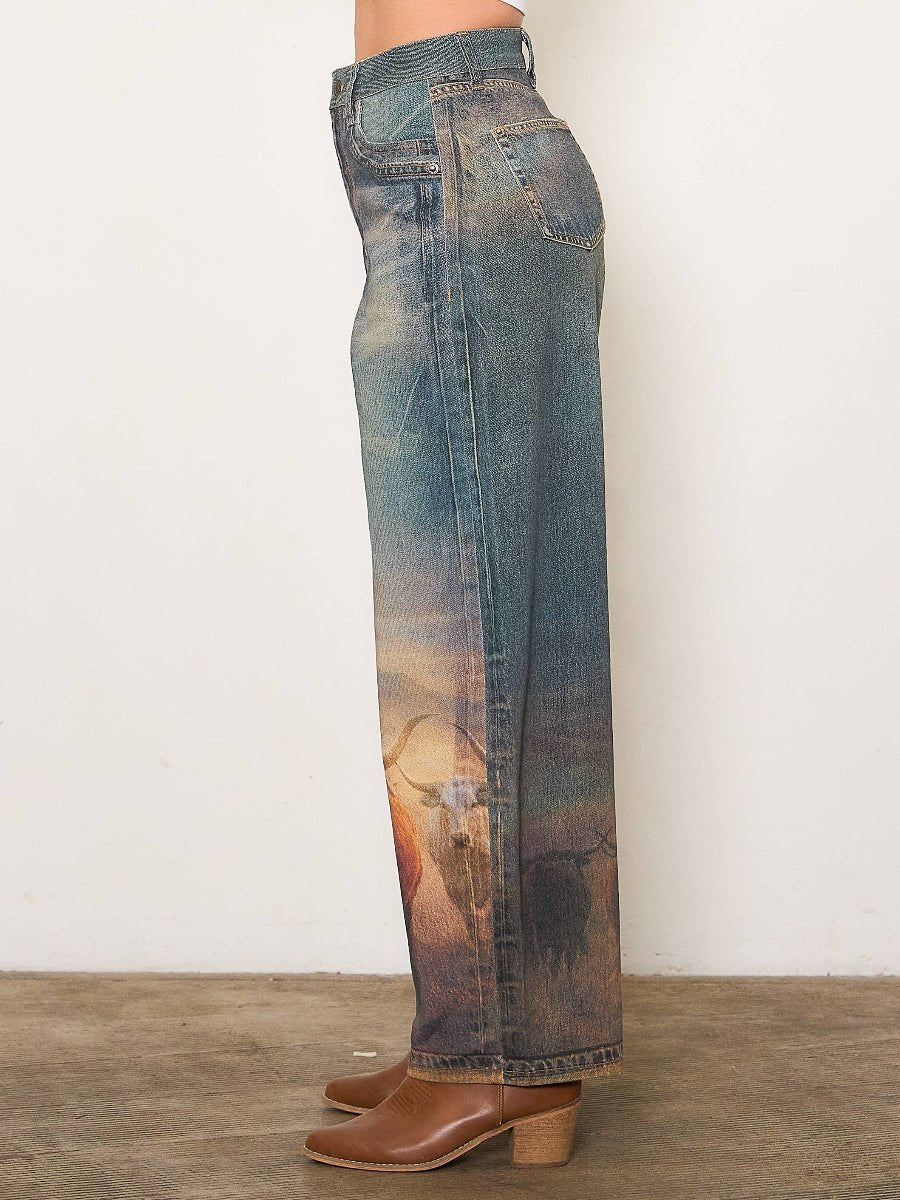 Denim jeans with a scenic print worn by a person on a wooden floor.