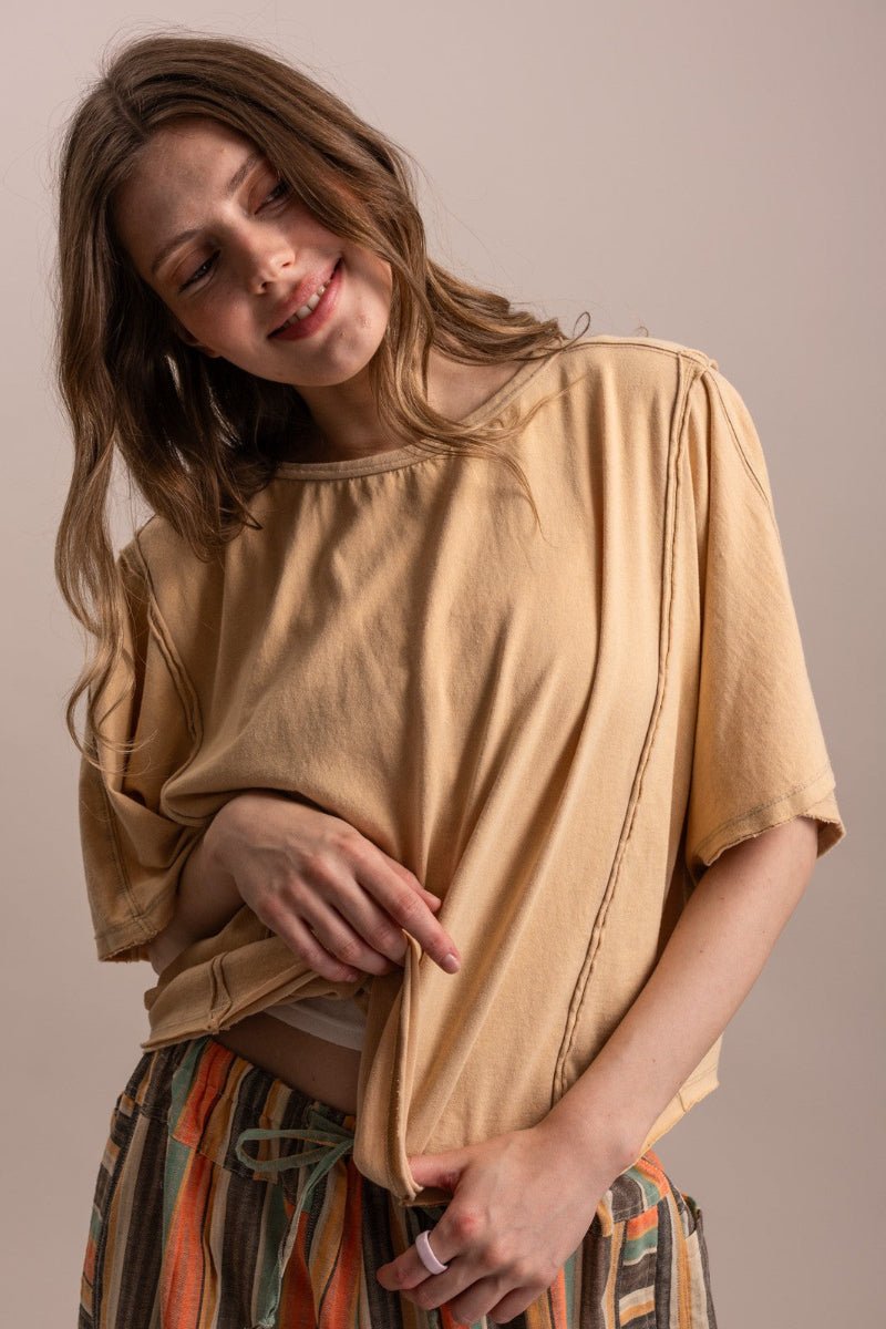 A woman wearing a loose, short-sleeved tan top and striped pants, posing against a solid beige background.