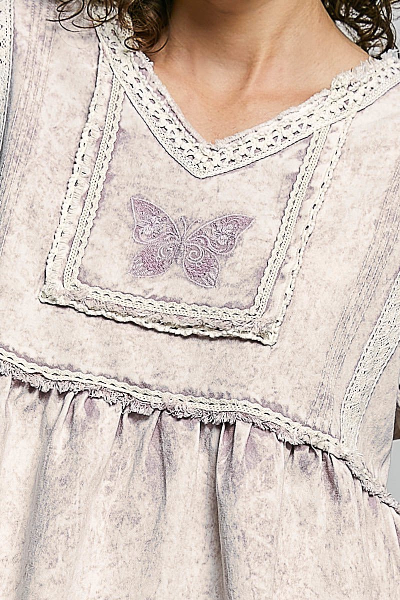 Close-up of a light purple dress with lace details and a butterfly design.