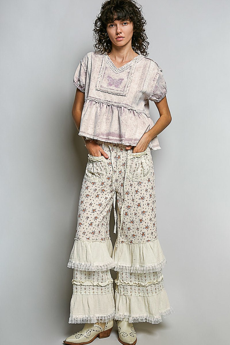 Woman wearing a floral top and tiered pants against a plain background