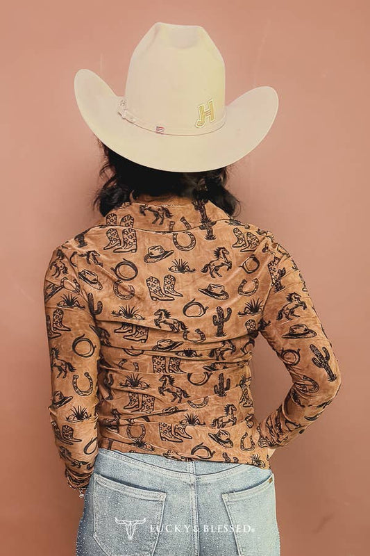 A person shown from the back wearing a tan long-sleeve shirt with a black western-themed print, a cream cowboy hat