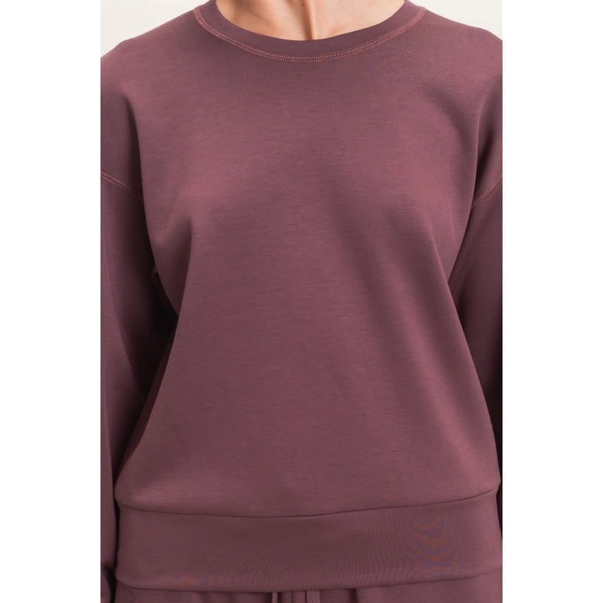 A close-up of a person wearing a crewneck sweatshirt in a dusty mauve or muted plum color, paired with matching bottoms.