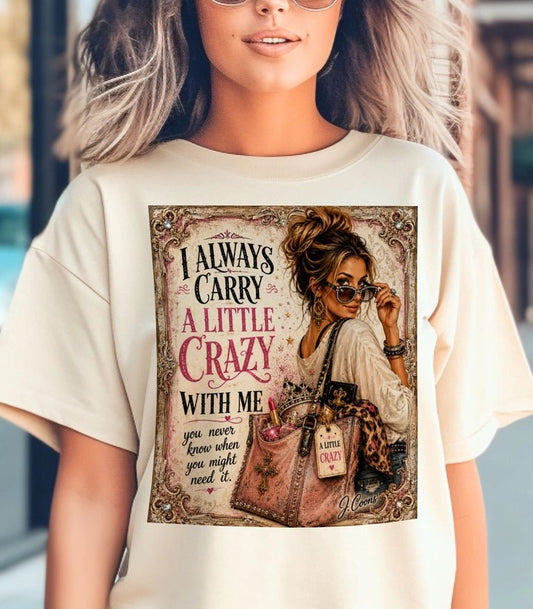 A woman wearing a cream-colored oversized t-shirt with a large graphic print on the front. The graphic features an illustration of a stylish woman with sunglasses, a handbag, and the text 'I ALWAYS CARRY A LITTLE CRAZY WITH ME'.