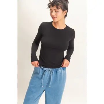 A woman wearing a fitted black long-sleeve crewneck top and light blue drawstring sweatpants, standing against a plain light background.
