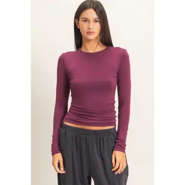Woman wearing a purple long-sleeve top and dark pants on a light background