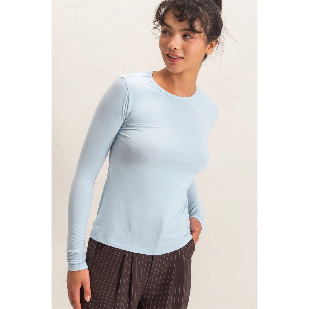 woman wearing a light blue top and brown pants with her hand in her pocket