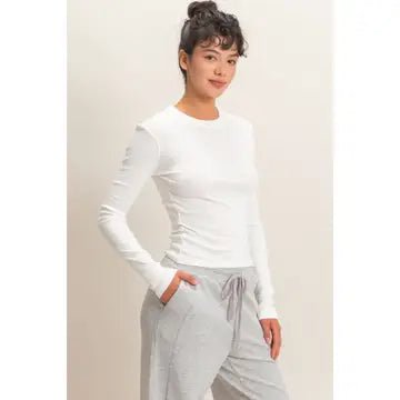 Woman wearing a white long-sleeve top and gray pants against a plain background