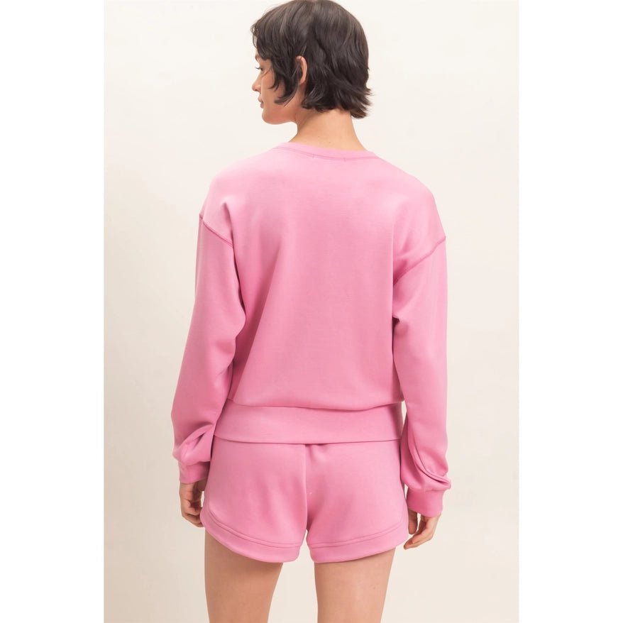 A model shown from the back wearing a matching pink sweatshirt and shorts set against a plain off-white background.