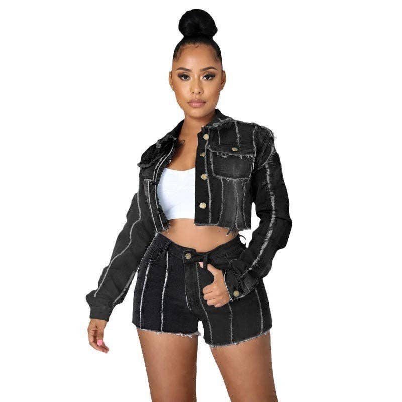 A woman modeling a cropped black denim jacket and matching frayed denim shorts over a white crop top, photographed against a plain white background.