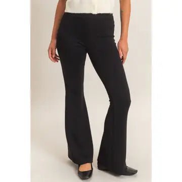 Black flared pants worn by a model, paired with a white top and black shoes, shown against a plain light background.