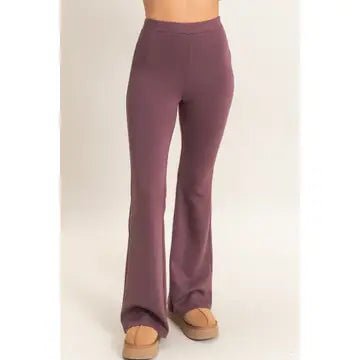 A person wearing high-waisted, straight-leg or bootcut pants in a muted mauve-purple color, paired with tan flat shoes, shown from the waist down against a plain light background.