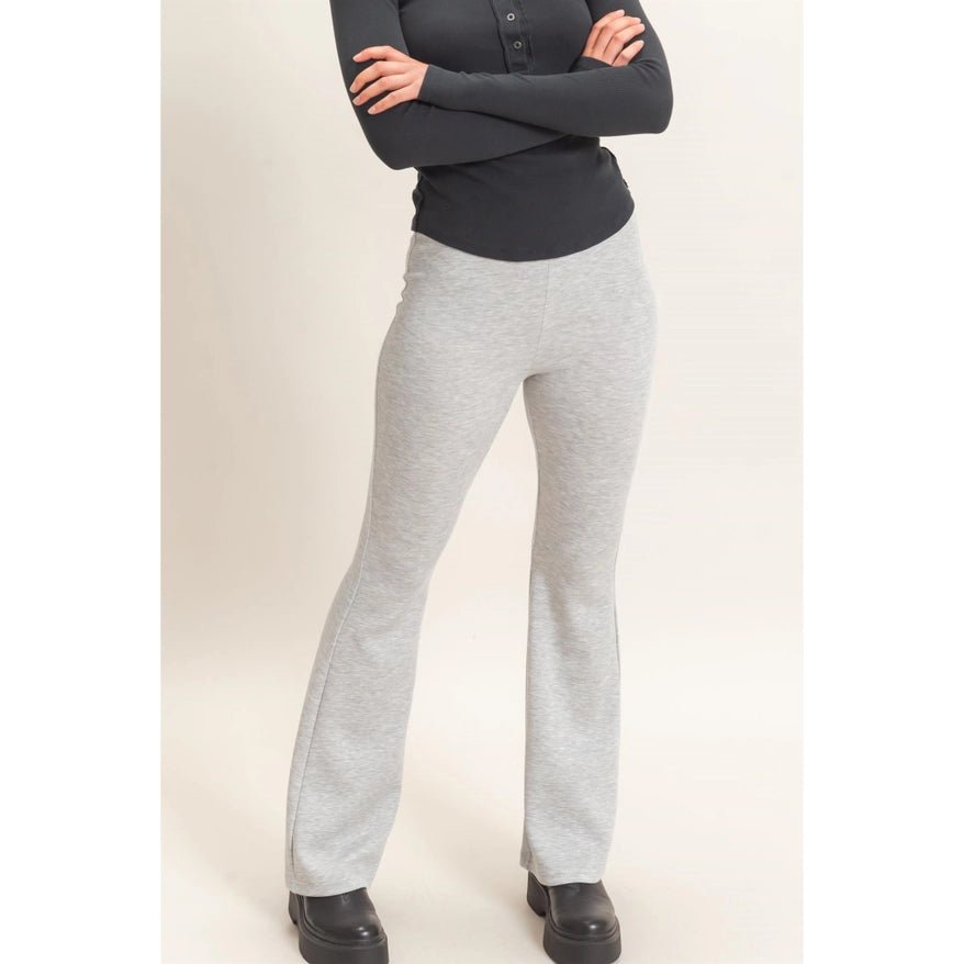 A model wearing light heather gray flared sweatpants and a black long-sleeve top, standing with arms crossed against a plain light beige studio background.