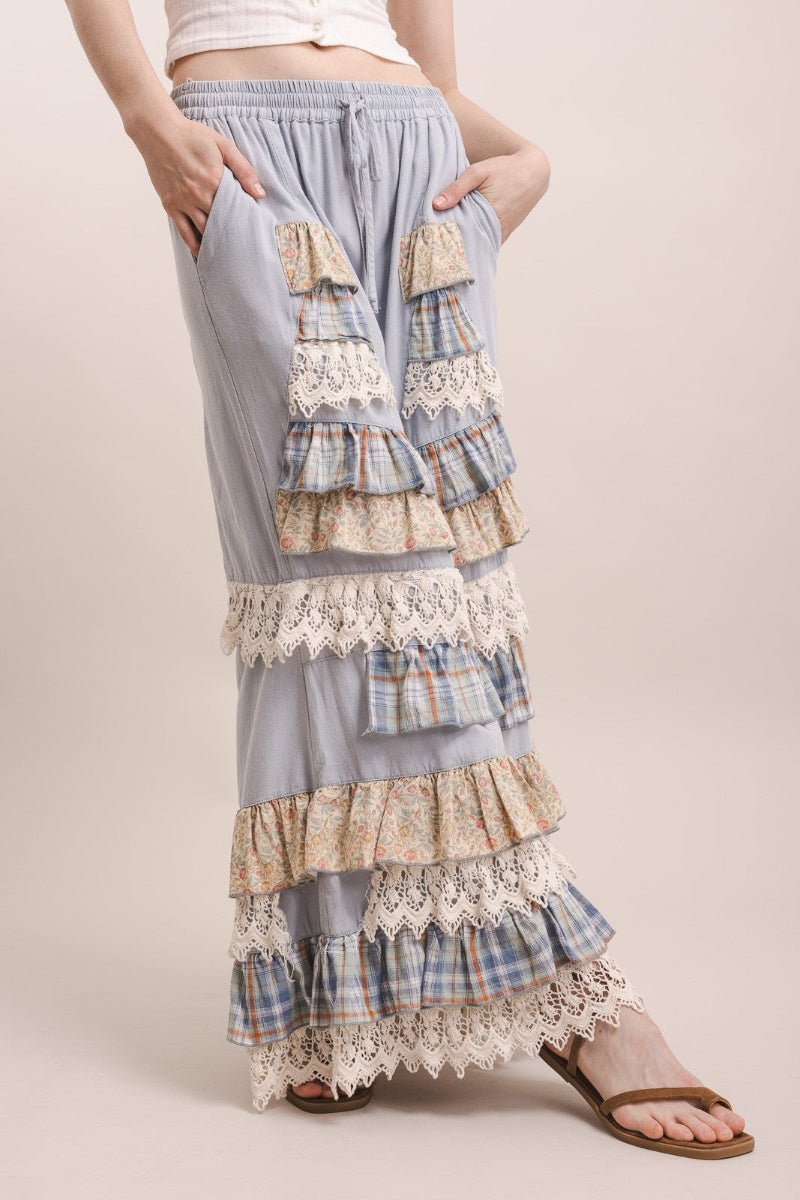 A person wearing a light blue maxi skirt with layered ruffles, lace trim, and patchwork plaid fabric panels, shown against a plain beige studio background.