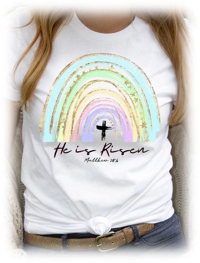 White t-shirt with rainbow design and 'He is Risen' text, worn by a person.