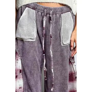 A close-up of a person wearing loose, wide-leg cropped pants in a washed mauve-purple corduroy-like fabric with large white textured front patch pockets and a drawstring waist.