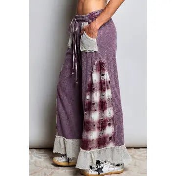 Purple wide-leg bohemian maxi pants with a tie-dye patch, lace ruffle hem, and drawstring waist, shown on a model.