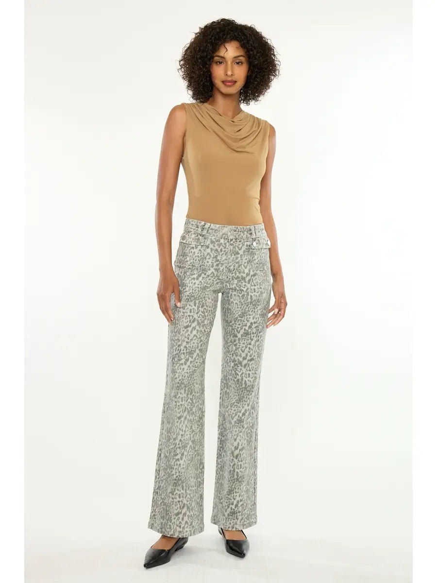 A woman modeling a sleeveless tan cowl-neck top and high-waisted, wide-leg gray pants with a light animal print, paired with black pointed flats, against a plain white studio background.