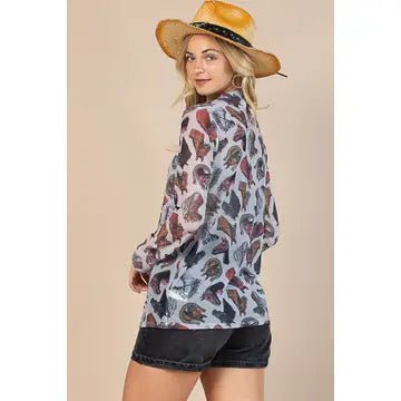 A woman wearing a long-sleeve butterfly-print blouse and denim shorts, posed from the back and wearing a straw hat against a solid beige background.