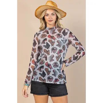 A woman modeling a long-sleeve mock-neck top with an all-over cowboy hat pattern, paired with black denim shorts and a straw cowboy hat, set against a solid beige background.