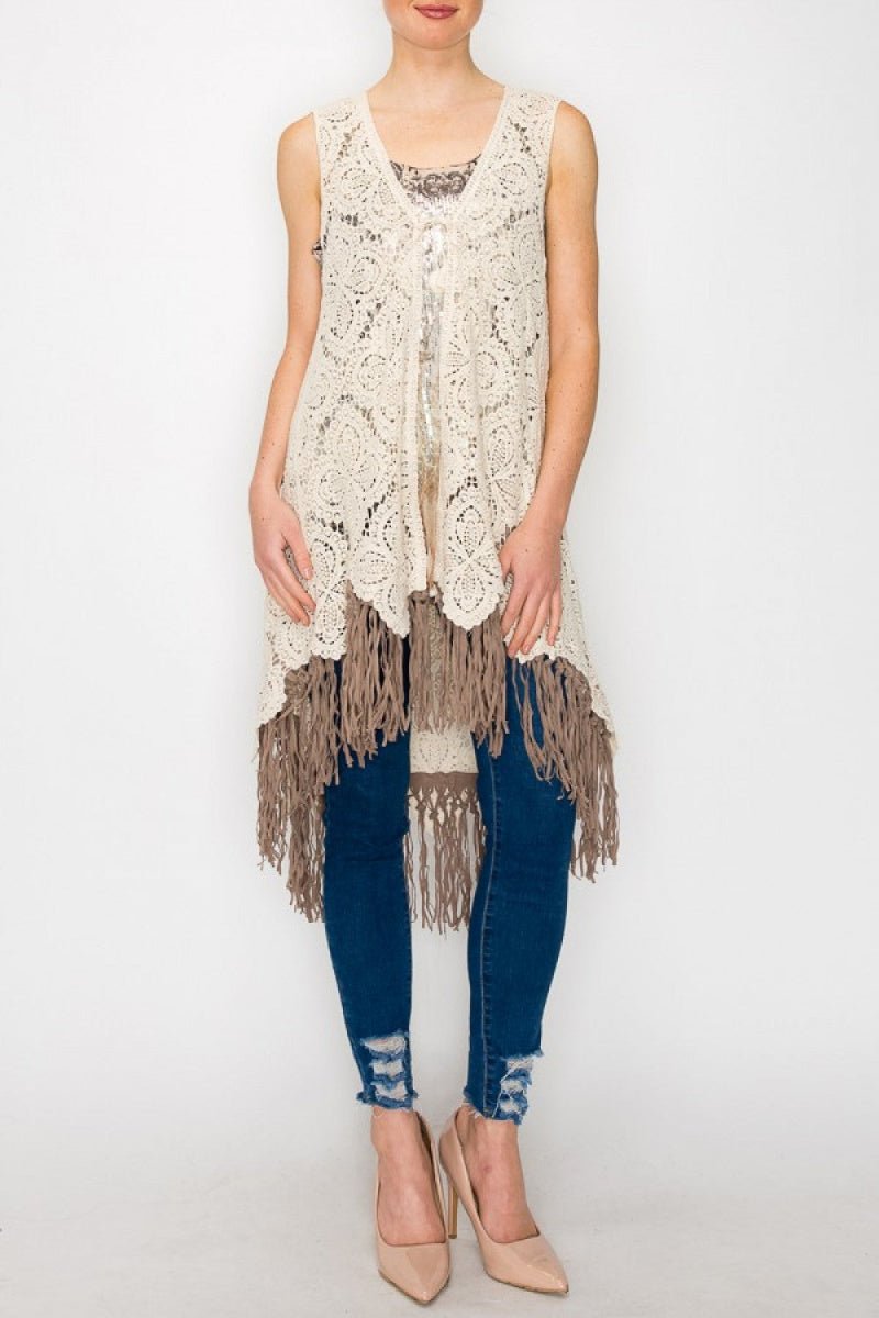 Woman wearing a sleeveless crochet top with fringe and blue jeans on a white background