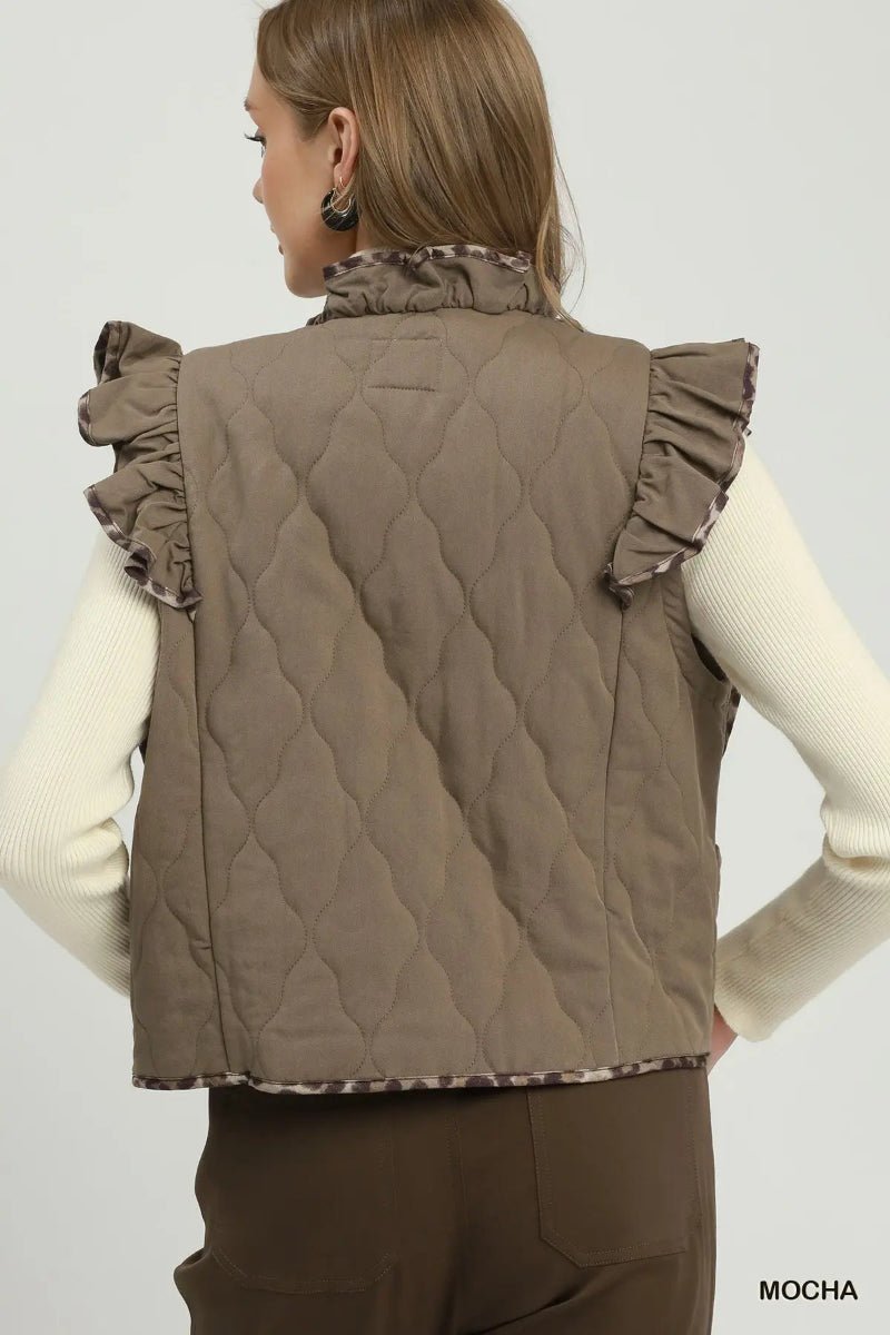 A woman shown from the back wearing a taupe-brown quilted sleeveless vest with ruffled shoulder details and a patterned ruffled collar, over a cream ribbed long-sleeve top and brown pants. The word 'MOCHA' appears in the bottom right corner.