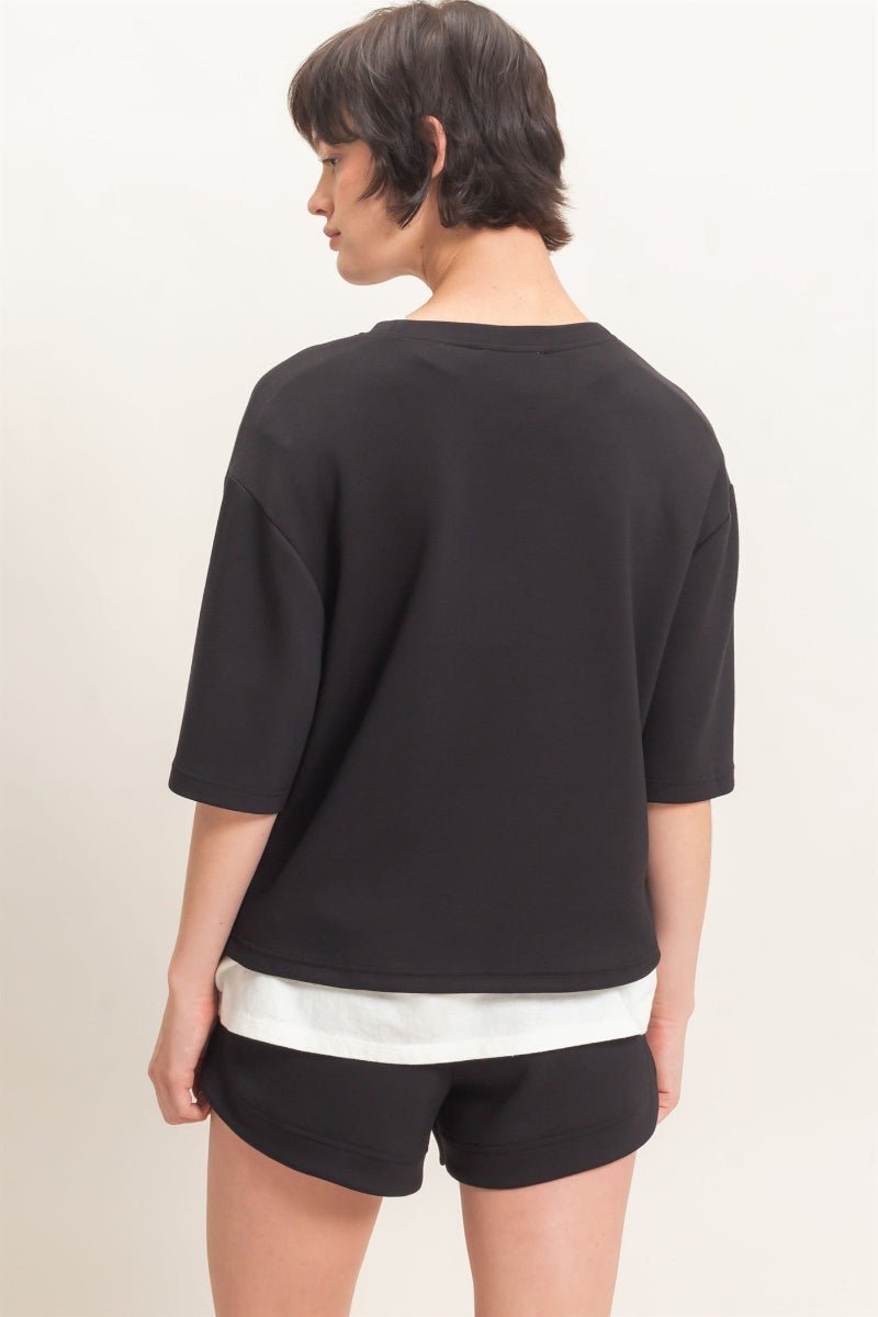 Person wearing a black oversized shirt and black shorts with white trim on a beige background
