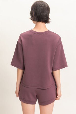 A model shown from the back wearing a matching mauve-colored short-sleeve top and shorts set against a plain off-white background.