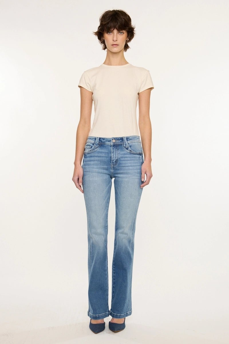 A model stands against a plain white studio background wearing a light beige short-sleeve crewneck t-shirt and light-wash blue flare jeans with dark blue heels.