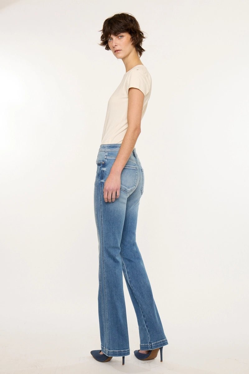 A model wearing light-wash blue flare jeans, a cream short-sleeve t-shirt, and dark blue heels, shown from a side profile against a plain white studio background.