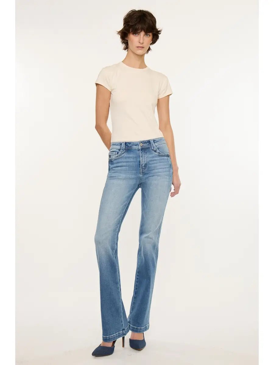 A model wearing a cream short-sleeve t-shirt, light-wash blue high-rise flare jeans, and dark blue heels, standing against a plain off-white studio background.